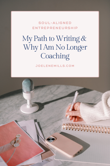 a photo of a woman's hand writing in a notbook with a pink phone and microphone on her desk. Th words "soul-aligned entrepreneurship, my path to writing and why I am no longer coaching" overlayed