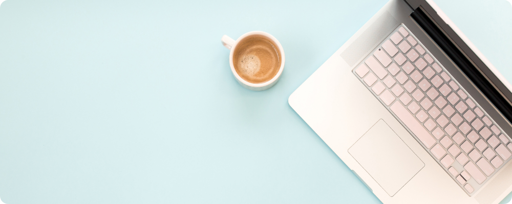 Clean desk with laptop and coffee on pastel blue surface, representing simple, structured blog posts for coaches.