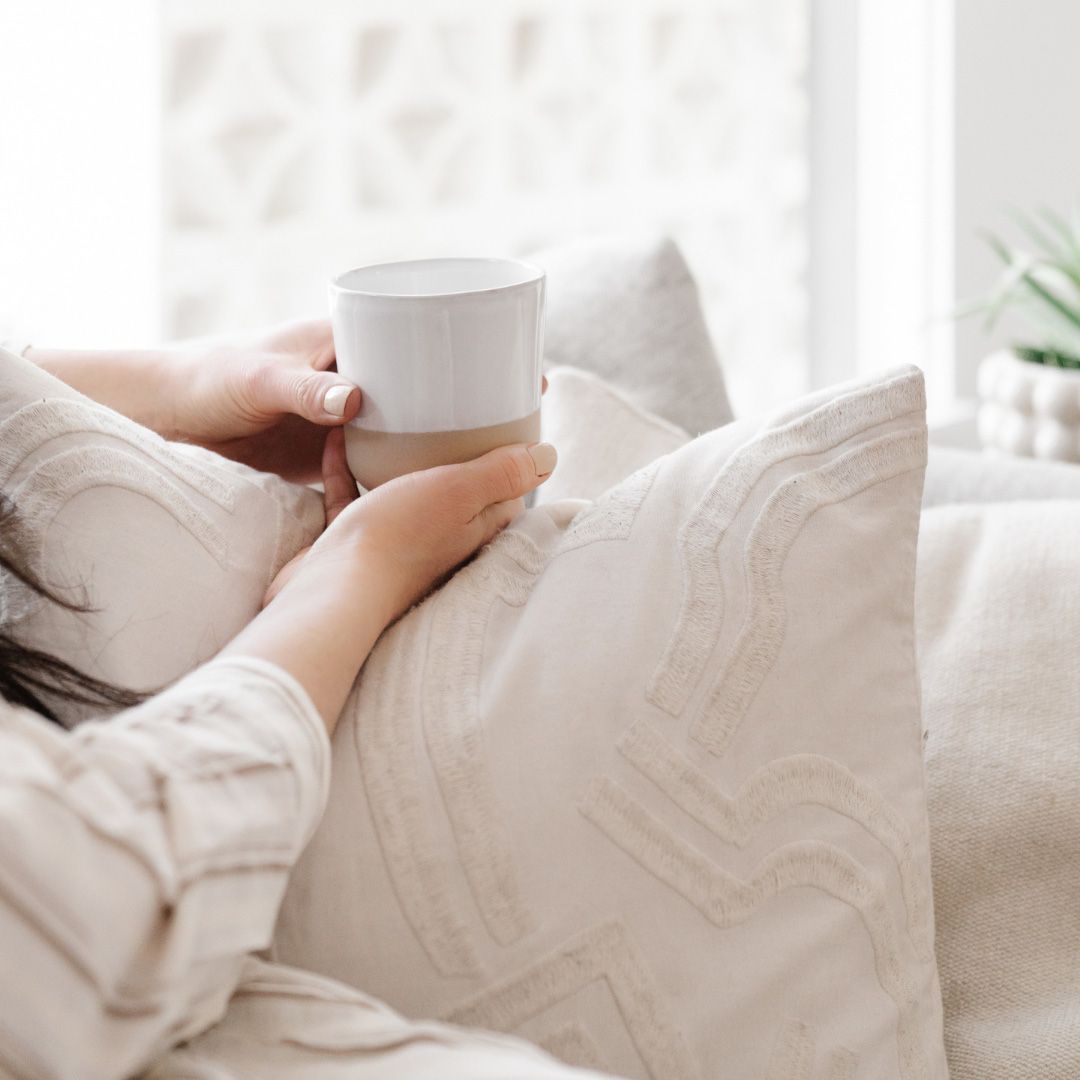 Woman holding a cup of coffee and a pillow.