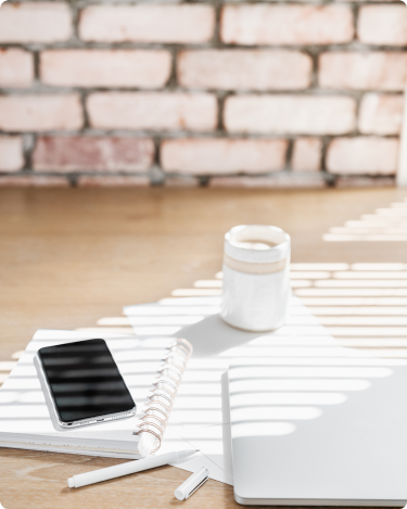 Sunlit desk with notebook, phone, and laptop. A calm blogging setup to plan blog post ideas and give your blog page a clear job.