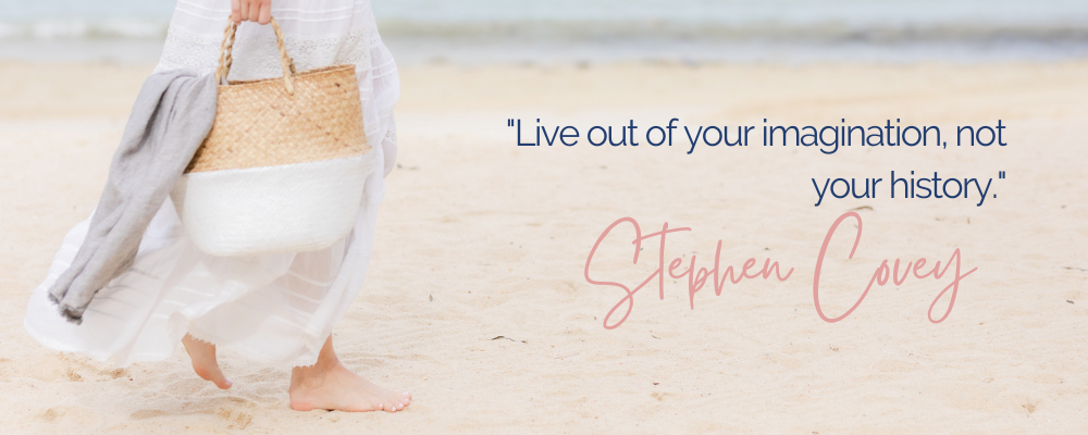 Woman walking barefoot along the beach carrying a white and wicker beach bag with the quote "Live out of your imaginatin, not your history" by Stephen Covey