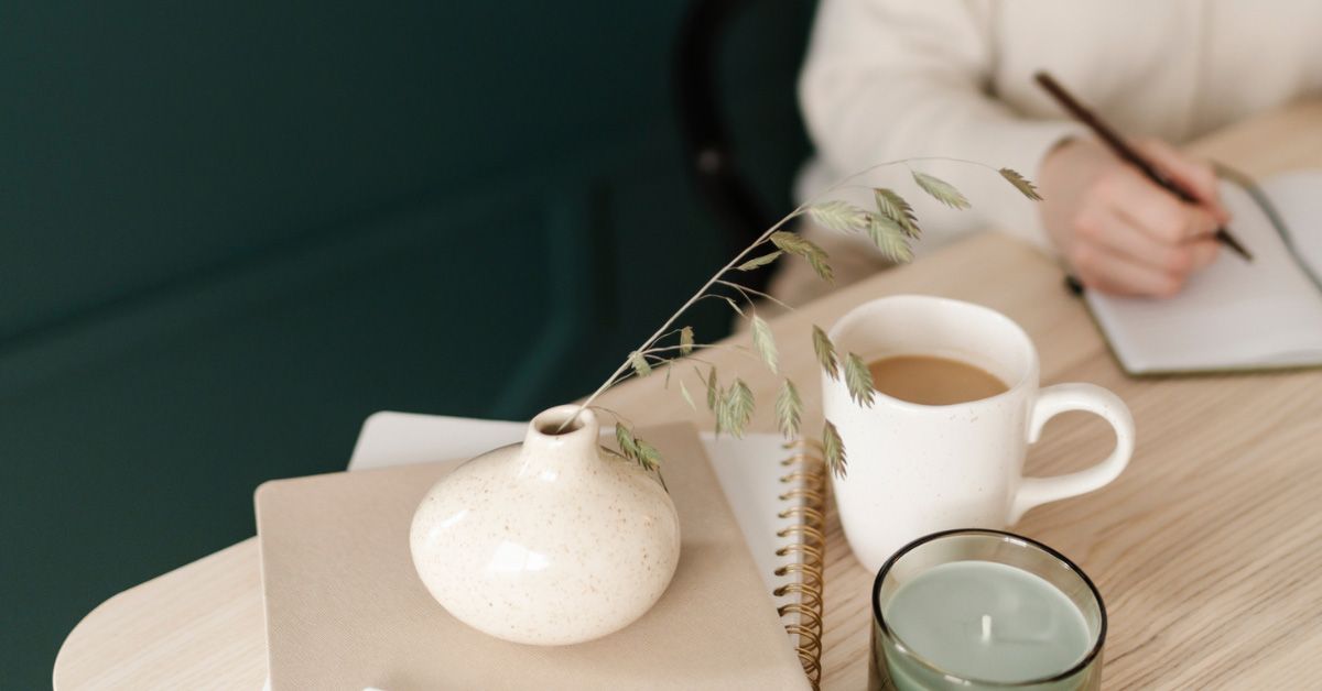 A vase on top of notebooks, on a desk, where a woman is drinking coffee and writing in her journal reflecting on 2024