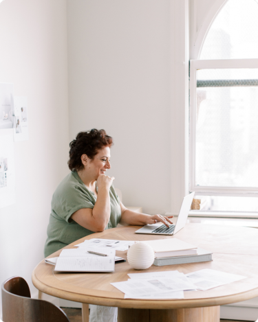 Introverted coach smiling while working on laptop at home office table — quiet productivity and simple blogging habits in action.