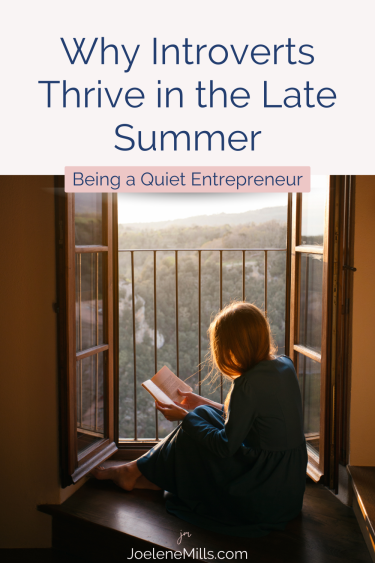 A woman sitting quietly in a window, reading a book at sunset with the words "Why introverts thrive in the late summer"