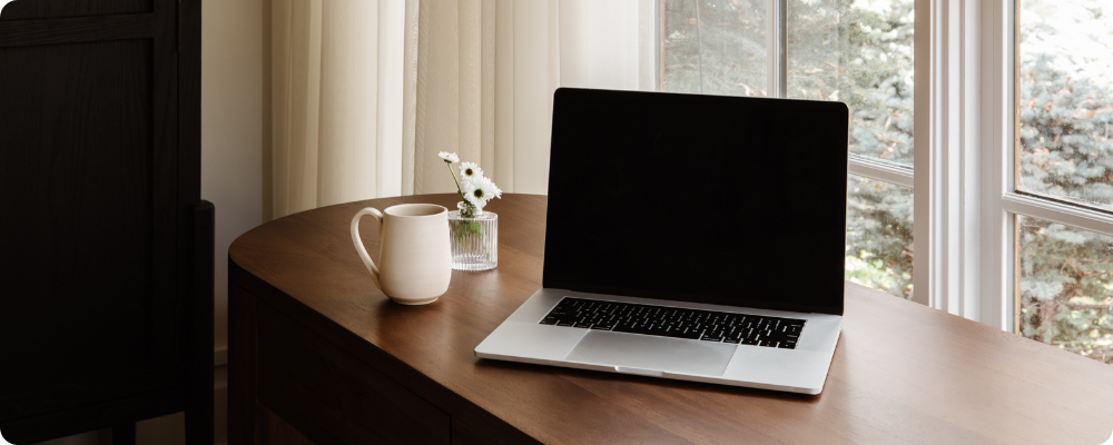 Close-up laptop, coffee mug, and flowers on wooden desk, simple blog tools for writing a blog post.