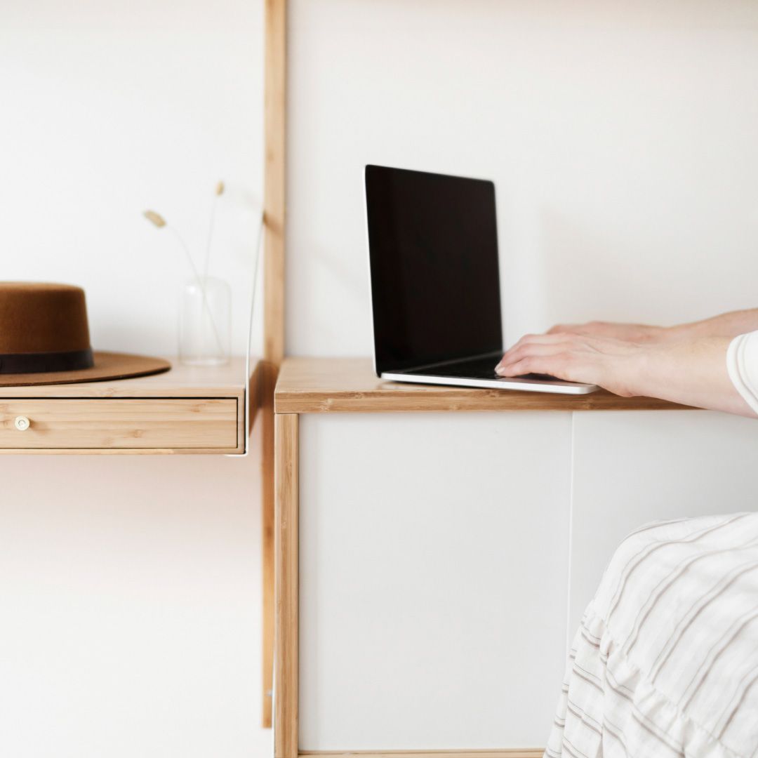 Photo of a woman typing on her laptop, with a brown felt hat on her desk