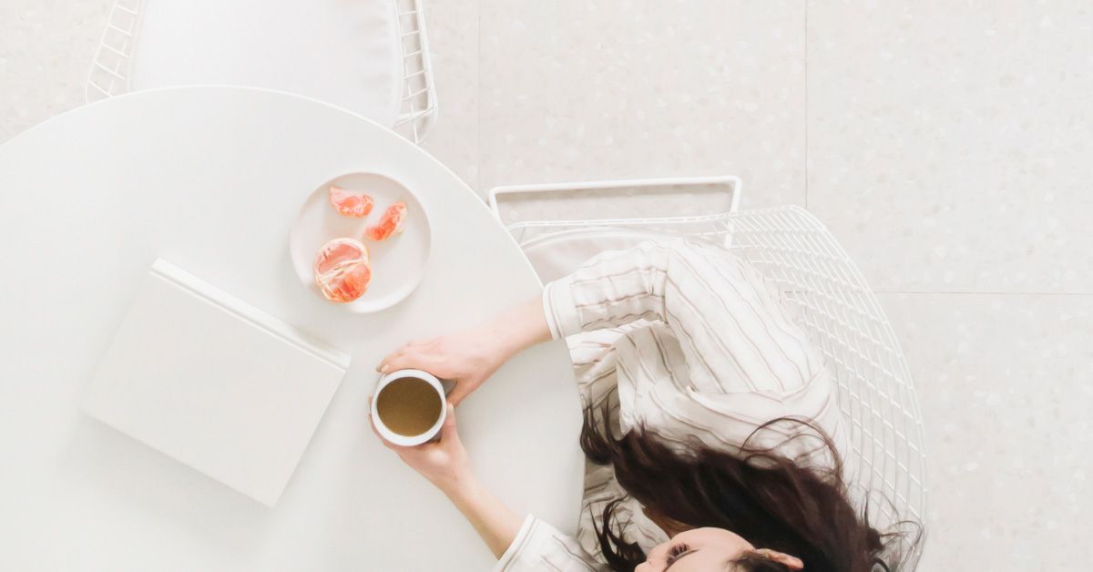 Top View of a woman sitting alone at a table with a cup of coffee, orange, and notbook