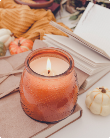 Lit fall candle with notebooks, pumpkins, and a cozy sweater—representing fall business clean-up and simplifying before Q4.