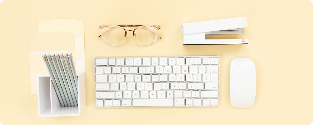 Flat lay of minimalist workspace with keyboard, pencils, and glasses on yellow background — calm blogging productivity setup for coaches.