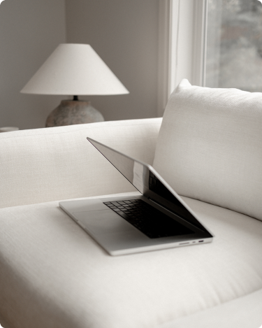 Open laptop on a neutral couch by a window and lamp, a calm setup for writing a blog post and updating your blog page.