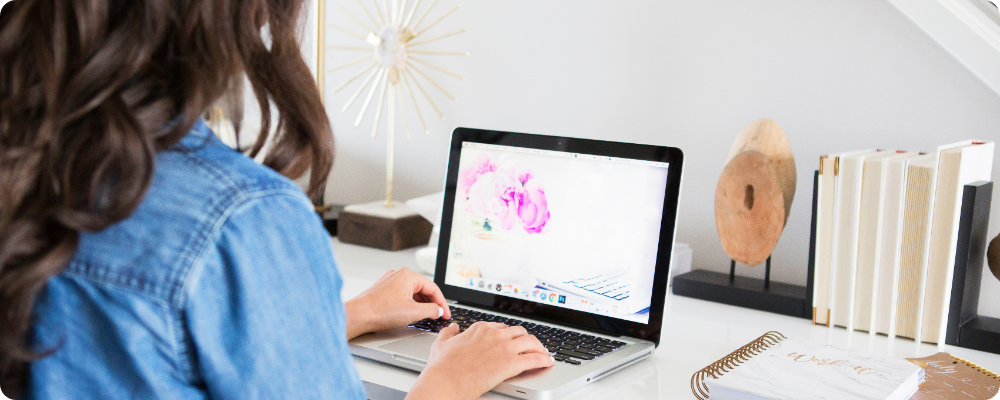 Woman typing on laptop at bright white desk, writing evergreen blog posts for her coaching business, calm workspace setup.