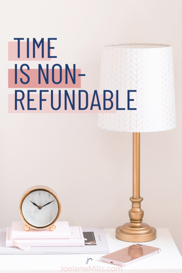 photo of a clock on a bedside table with a lap, notebooks and a pink phone. The words "time is non-refundable" 