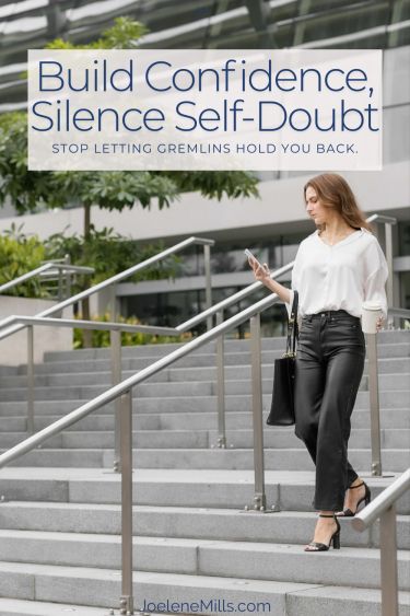 Woman walking down a set of stairs outside an office building, lookingat her phone with the words build confidence silence self-doubt