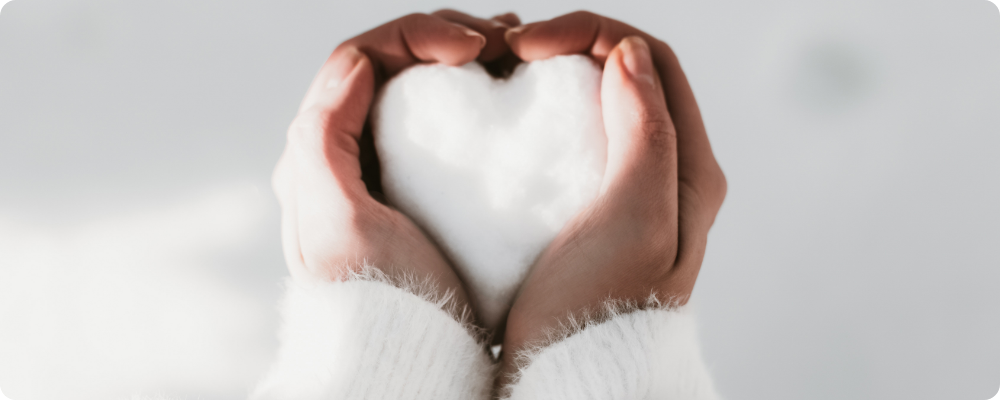 Soft winter light on hands holding a heart-shaped snowball, reflecting trust, connection, and quiet selling for coaches.