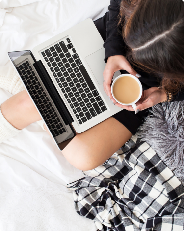 Woman sitting in bed with laptop and coffee, reviewing blogging stats and planning new blog post ideas for her coaching blog.